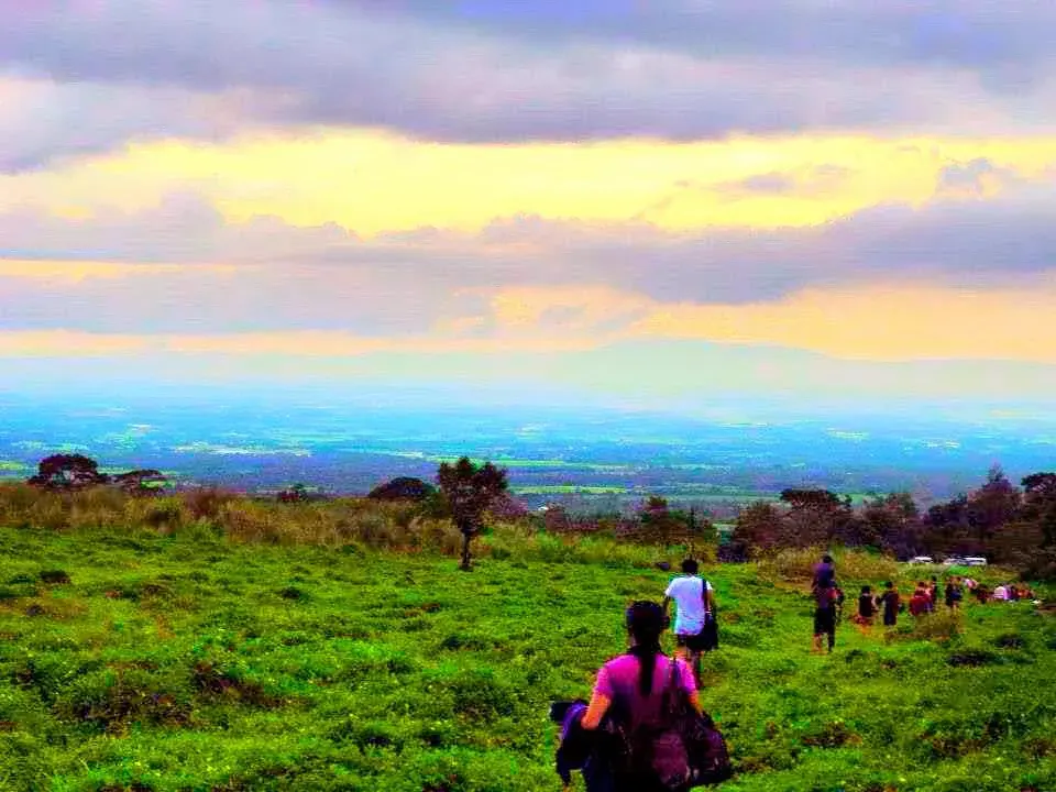 A group walking a grassy hillside overlooking a Bicol valley
