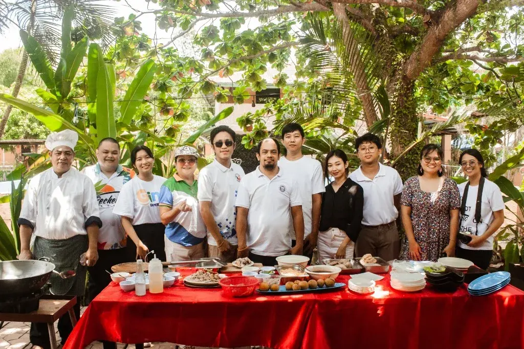 A chef and a tourism team gathered behind a table of local dishes under tropical trees